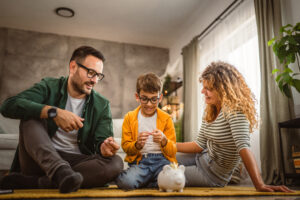 mam dad and son sit on the carpet,floor and save money in the piggy bank at home
