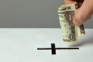 Man puts donation in his hand with dollar in slot in the form of Christian cross. Copy space for text